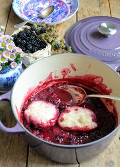 a pot filled with berries and ice cream on top of a wooden table next to flowers