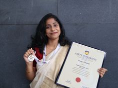 a woman holding up an award plaque in front of a gray wall and wearing a white sari