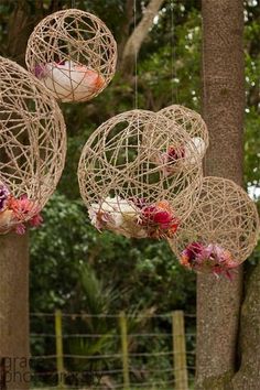 three hanging baskets with flowers on them in front of some trees and fenced in area