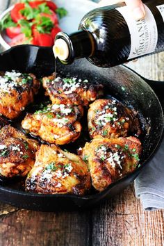 someone pouring wine into a skillet filled with chicken wings and garnished with parmesan cheese