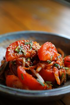 a bowl filled with tomatoes and onions on top of a wooden table next to rice