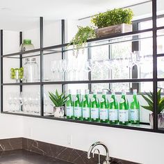 a kitchen sink sitting under a mirror next to a counter with bottles and glasses on it