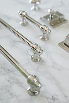 four chrome handles on a white marble counter top with metal pulls and knobs in the middle