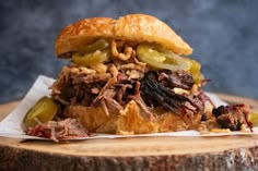 a roast beef sandwich with pickles and onions on a piece of wood, ready to be eaten