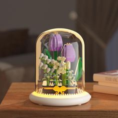 a glass case with flowers in it on top of a table next to a book