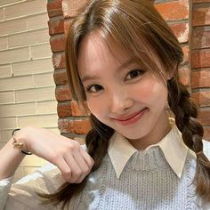 a girl with long hair wearing a white shirt and smiling at the camera while standing in front of a brick wall