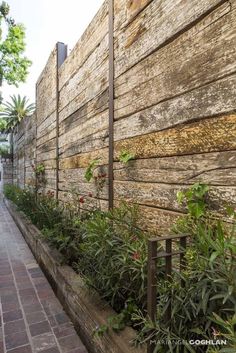 an alley way with plants growing on the wall and brick walkway between two buildings that have wooden slats attached to them