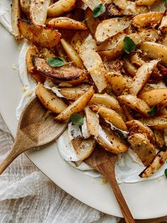 a white plate topped with potatoes covered in cheese and herbs next to a wooden spoon