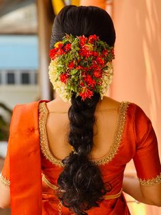 a woman with flowers in her hair wearing an orange sari and red blouse on