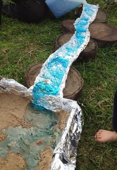 a person standing in the grass next to a small stream made out of tin foil