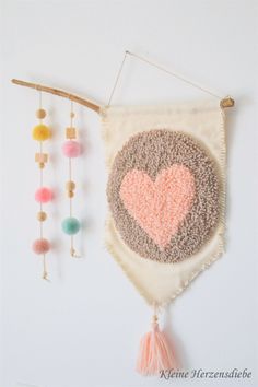 the wall hanging is decorated with beads, tassels and a heart on it