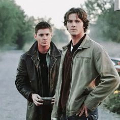 two young men standing next to each other in the street, one holding a cup