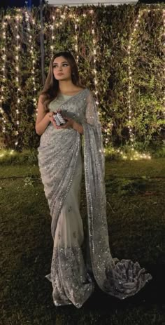 a woman wearing a sari standing in front of a wall with lights on it