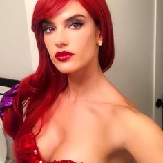 a woman with long red hair and bright makeup is posing in front of a mirror