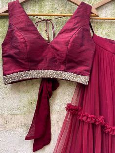 A three-piece burgundy tier ruffle lehenga set from the Priti Sahni collection. This raw silk burgundy ruffle tier lehenga is paired with a deep neck burgundy blouse in raw silk fabric with sequin-pearl detail. The lehenga has side hanging tassels to the waistline. And the blouse has a ghungroo tassel and ribbon tie-up at the back. The outfit is completed with a burgundy sequined butti work net dupatta with scalloped edging. Designer Ruffled Sets For Navratri, Festive Red Sharara With Ruffles, Designer Silk Sets With Ruffles, Festive Red Lehenga With Ruffles, Red Ruffled Sharara For Wedding, Red Ruffled Sharara For Diwali, Festive Silk Ruffled Choli, Organza Choli With Ruffles For Diwali, Festive Silk Choli With Ruffles