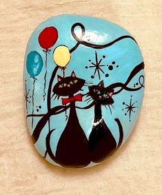 a painted rock with two cats and balloons