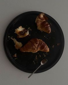 two croissants on a black plate with a spoon next to it and another piece of bread in the middle