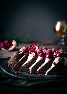 a chocolate cake with white frosting and raspberries is on a black plate