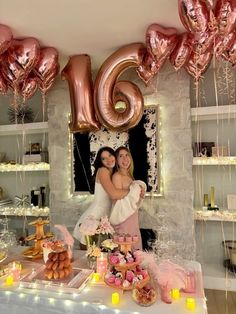 two women standing next to each other in front of a table with balloons and decorations