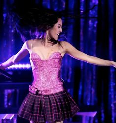 a woman in a pink corset on stage with her arms spread wide open