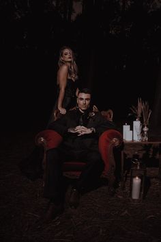 a man and woman are sitting on a red chair in the middle of a dark forest