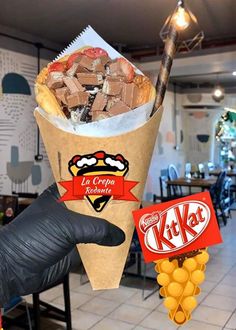 a person holding up a paper cone filled with candy and other items in front of a restaurant