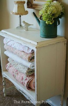 an old dresser with towels stacked on it and a watering can sitting on top of it