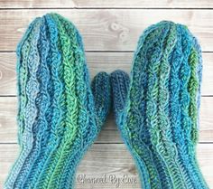 two blue and green knitted mittens sitting on top of a white wooden floor