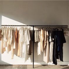 a rack with clothes hanging on it in front of a wall and floor next to a window