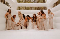 a group of women standing next to each other in front of a white wall and trees