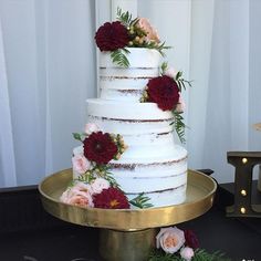 a three tiered wedding cake with red and pink flowers on the top is sitting on a gold platter