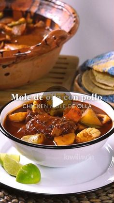 a bowl of stew on a plate with limes next to it and another dish in the background