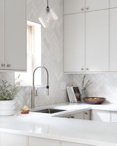 a kitchen with white cabinets and marble counter tops is pictured in this image, there is a bowl of fruit on the counter