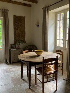 a dining room table with a bowl on it in front of two chairs and windows