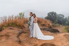 a man and woman standing on top of a dirt hill next to each other with flowers in their hair