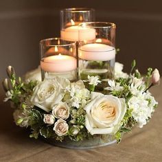 three candles are sitting on a table with flowers and greenery