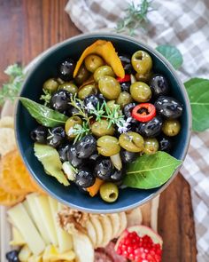 a blue bowl filled with olives, cheese and crackers on top of a wooden table