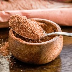 a wooden bowl filled with ground cinnamon on top of a table next to a spoon