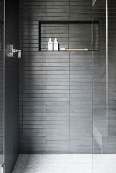 a bathroom with a glass shower door and white tile flooring, along with two shelves on the wall