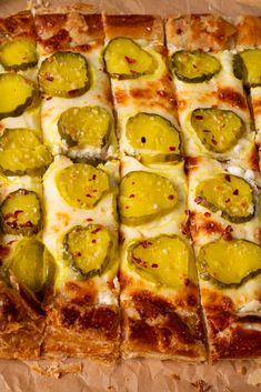 a square pizza with cheese and jalapenos cut into squares on top of brown paper