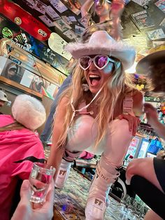 a woman in white clothes and sunglasses is dancing at a bar with other people around her