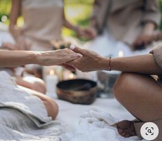 two women are holding hands while sitting on the ground with other people around them and candles in the background