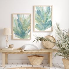 two paintings hang on the wall above a table with baskets and plants in front of it