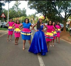 a group of women standing on the side of a road wearing colorful dresses and hats