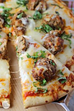 a pizza with meatballs and cheese cut into slices on a cutting board next to a fork