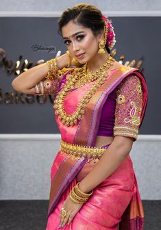 a woman in a pink and purple saree with gold jewelry on her neck, posing for the camera