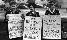 four people holding signs in front of a fountain