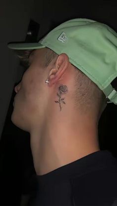 a man with a small rose tattoo on his left side behind the ear, wearing a green hat