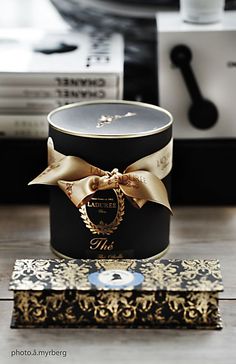 a black box with a gold bow on top of it sitting on a wooden table