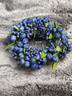 a wreath made out of blue berries and green leaves on top of a gray blanket